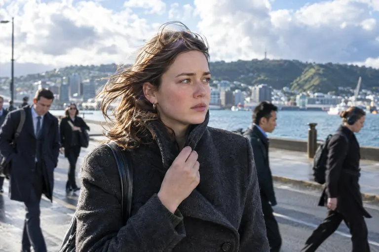 A woman in a wool coat walking along a windy harbour waterfront among commuters